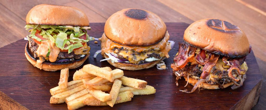 Classic, The Lot, and Bacon Burgers at Mutts Café Exmouth Classic, The Lot, and Bacon beef burgers with a serving of fries on a table outside Mutts Café Exmouth