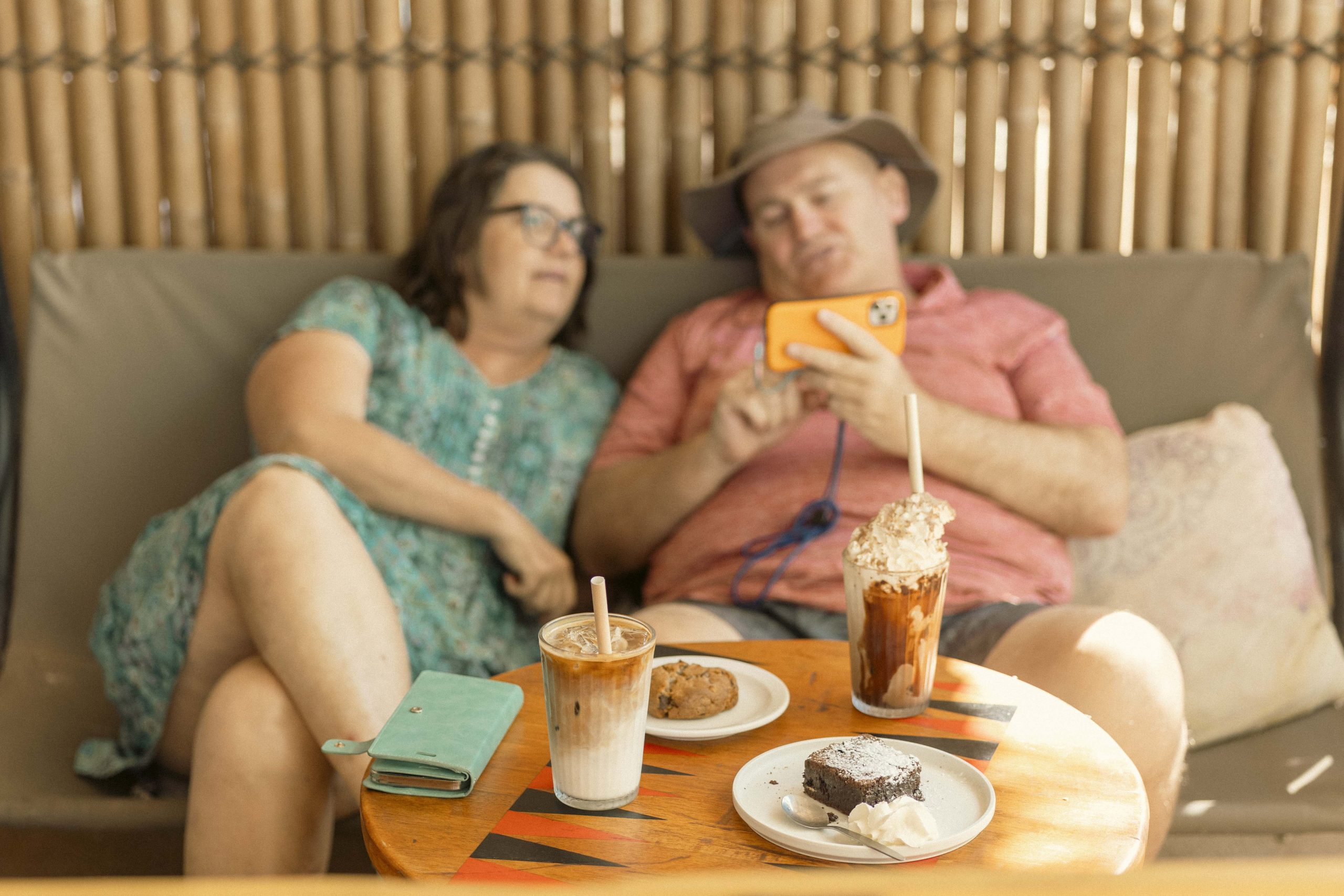 Relaxed Café Vibes in Exmouth | Mutts Café Couple relaxing on an outdoor couch at Mutts Café Exmouth with drinks, a cookie, and a brownie on the table in the sunshine.