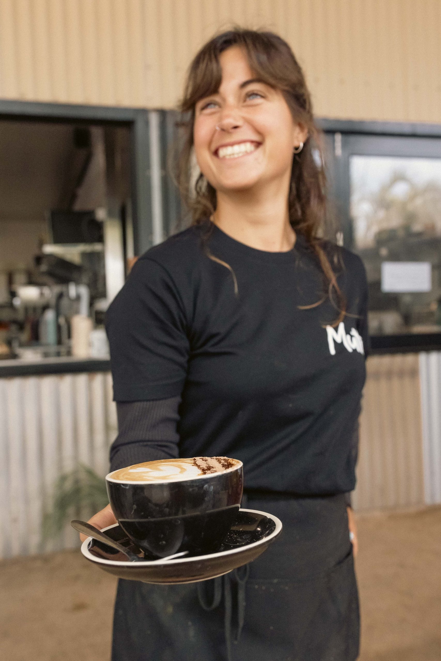 Hospitality jobs Exmouth WA. Friendly Service at Mutts Café Exmouth Staff member delivering coffee to a table at Mutts Café Exmouth, smiling and welcoming guests