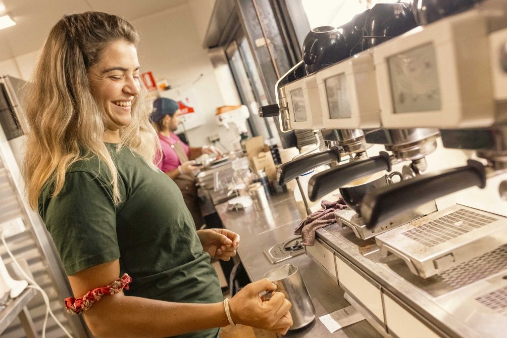 Smiling barista making coffee at Mutts Café Exmouth with sunshine streaming into the café. Contact Mutts Café Exmouth