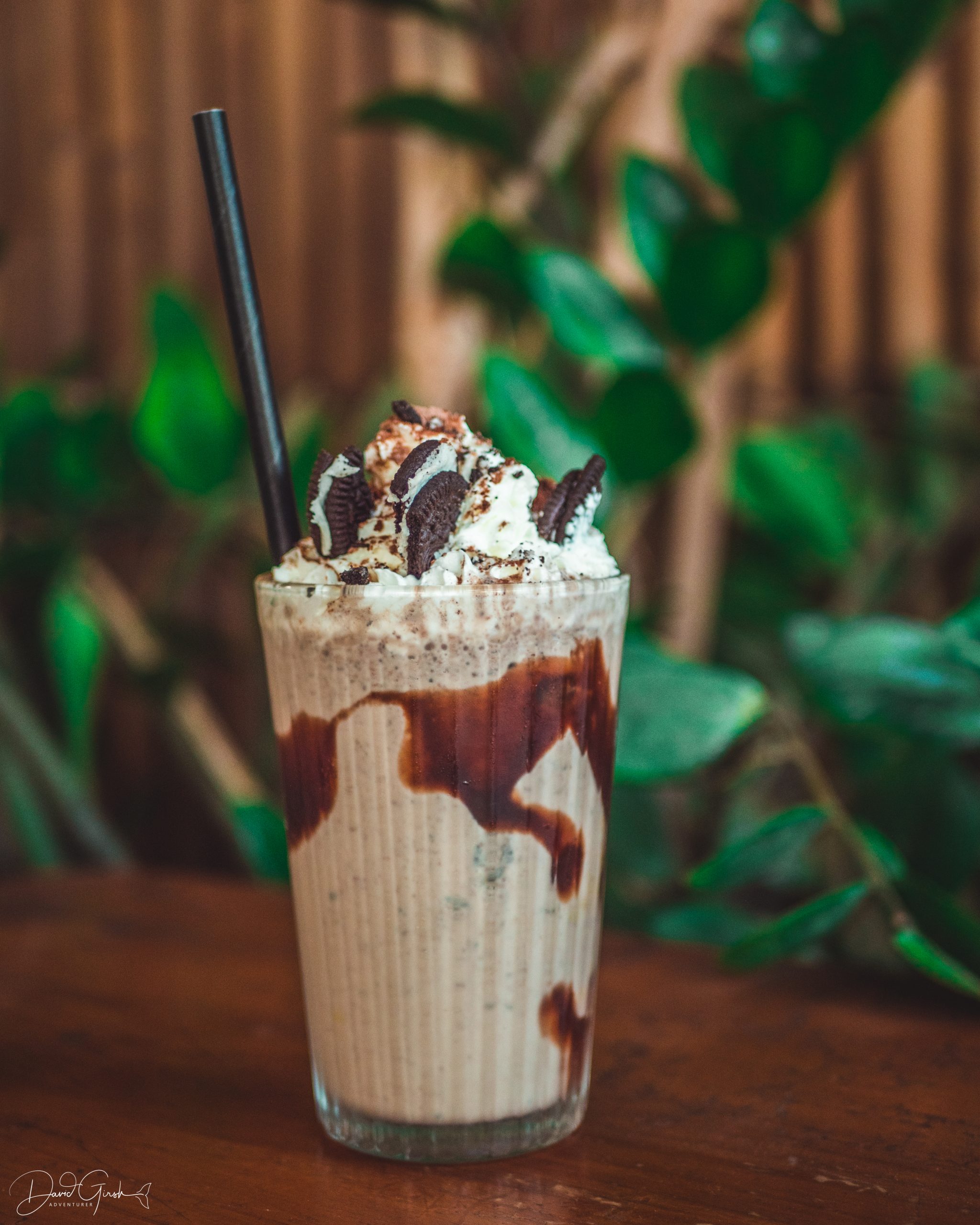 Close-up of loaded Oreo thickshake with cream and crushed Oreos, served outside at Mutts Café with greenery in the background. Drinks Menu Exmouth