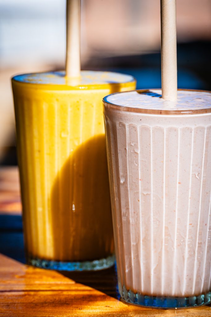 Mango Mojo & Pink Lady Smoothies at Mutts Café Two smoothies side by side — Mango Mojo and Pink Lady — served outside at Mutts Café on a hot summer day. Drinks Menu Exmouth