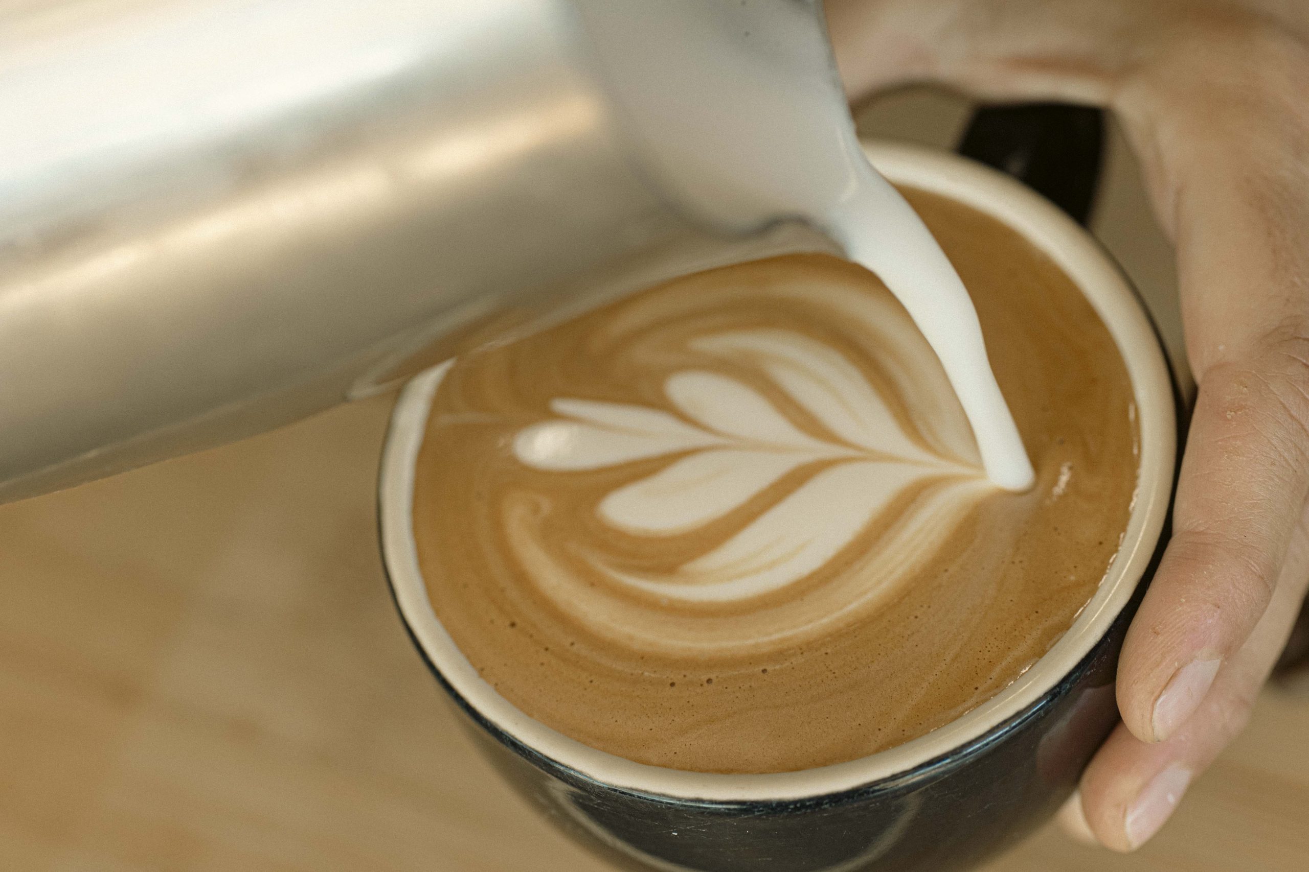 Mutts Café Latte Art Coffee Close-up of barista pouring milk into a freshly made latte with heart-shaped latte art. Drinks Menu Exmouth